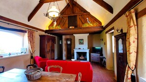 A dining area with a wooden table, red sofa, and a chandelier. - Le domaine des roseraies, Omaha Beach, Maupassant gîte (Monfréville)
