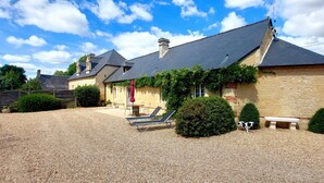 A stone building with a sloped roof, outdoor seating, and a gravel driveway. - Le domaine des roseraies, Omaha Beach, Maupassant gîte (Monfréville)