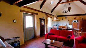 A cozy living room with a red sofa, a wooden table, and a kitchen in the background. - Le domaine des roseraies, Omaha Beach, Maupassant gîte (Monfréville)