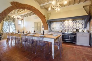 Un comedor con una mesa larga, sillas y una cocina con salpicadero decorativo y electrodomésticos.