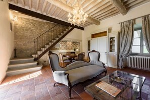 Un vaste salon agrĂ©mentĂ© dâun mur en pierre, dâun lustre, dâun canapĂ©, dâune table basse en verre et dâun escalier.