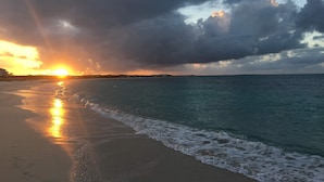 Une plage au coucher du soleil, avec des vagues et un ciel nuageux.