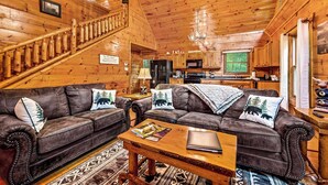 A cozy cabin interior with a wooden staircase, leather sofas with animal-themed pillows, a dining area, and a kitchen. - Wooded Smokies Hideaway • Arcade, Pool Table & Hot Tub (Sevierville)