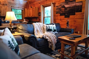 L’intérieur d’un chalet chaleureux, avec un canapé en cuir, une table basse en bois et une lampe.