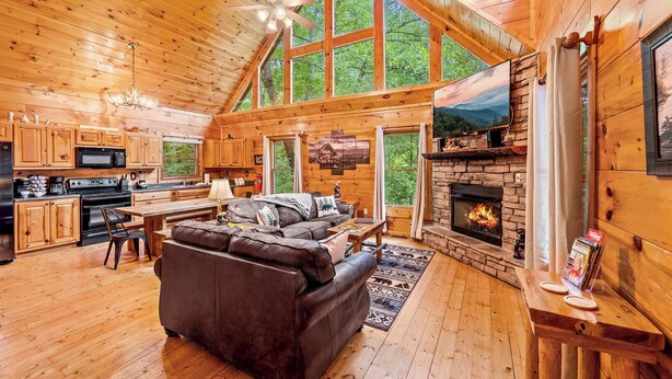 A log cabin interior with a fireplace, wooden floors, a sofa, and a kitchen area. - Wooded Smokies Hideaway • Arcade, Pool Table & Hot Tub (Sevierville)