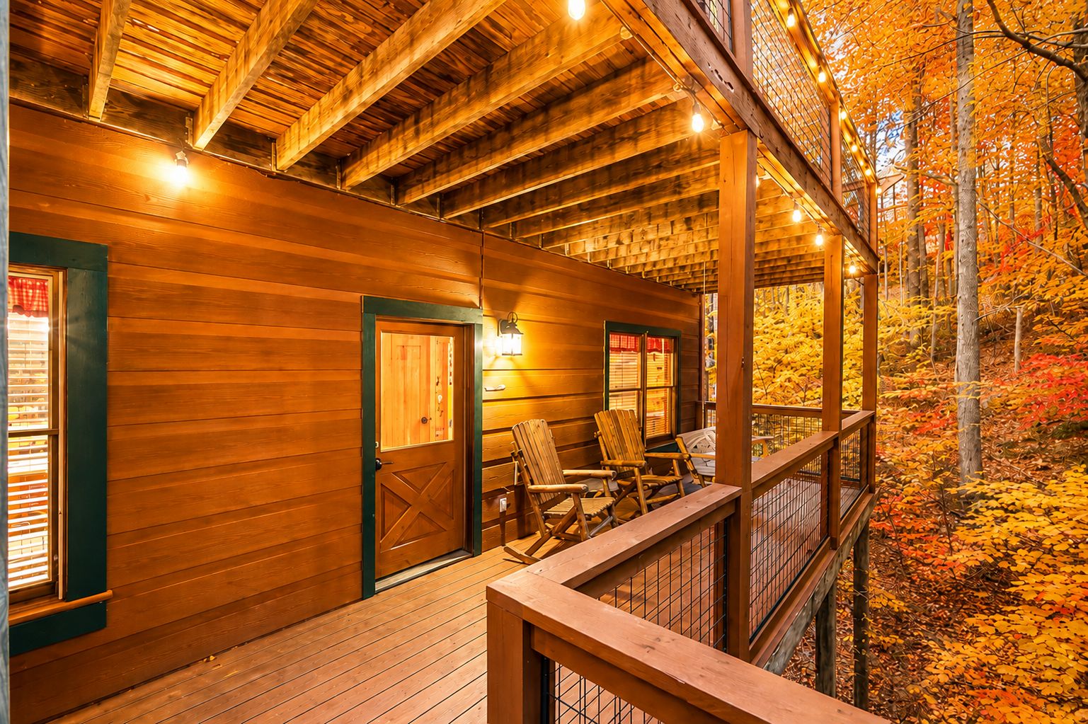 Une cabane en bois avec un porche, des chaises en bois et une vue sur le feuillage automnal.