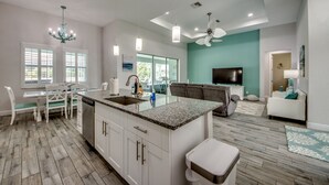A modern kitchen with a central island, white cabinetry, and a dining area with a white table and chairs.