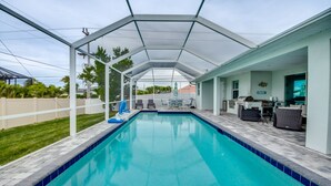 A covered swimming pool with a patio area, including seating and a kitchen.