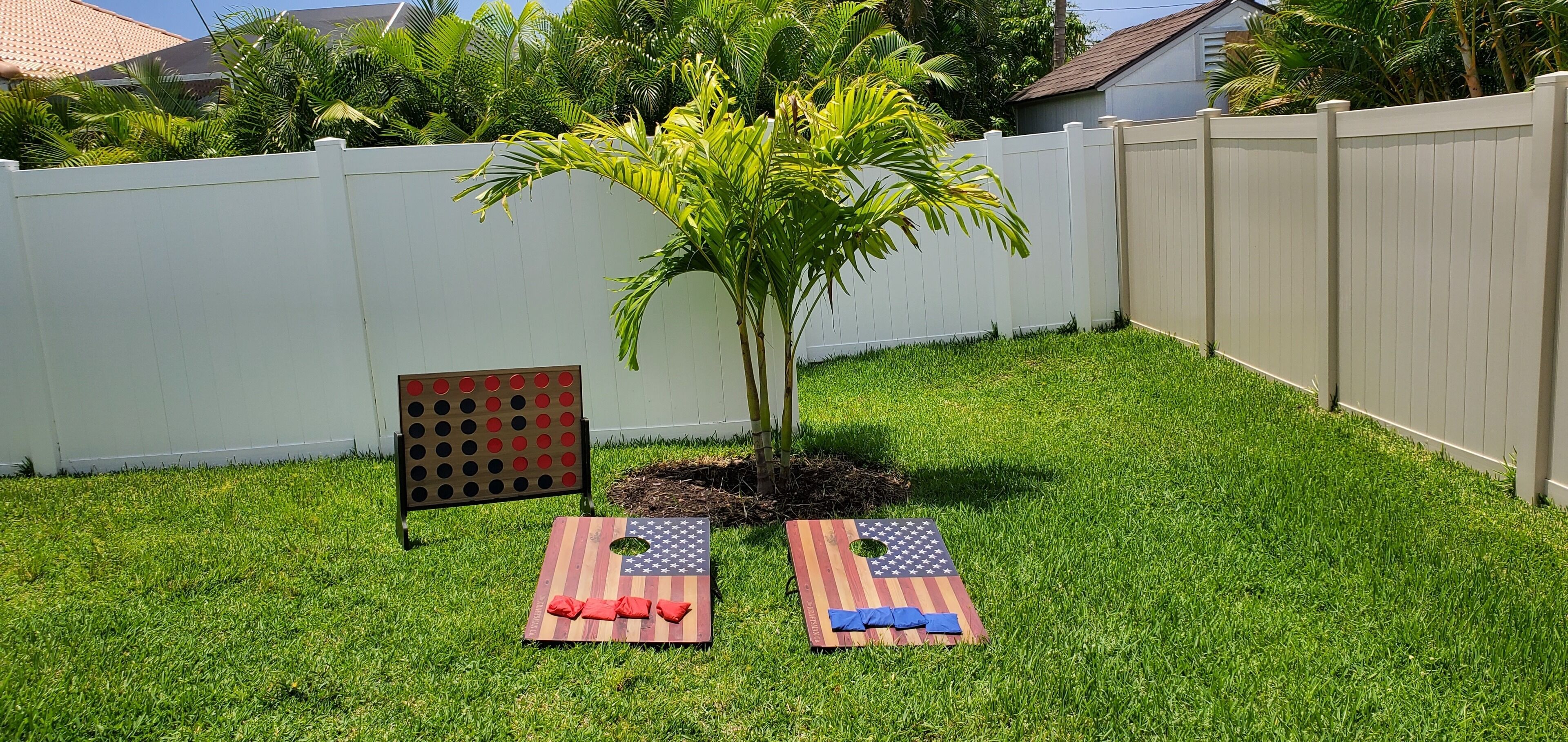 A backyard with a white fence, a small tree, and two American flag-themed bean bags.