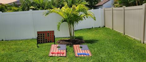 A backyard with a white fence, a small tree, and two American flag-themed bean bags.