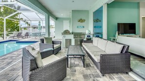 An outdoor patio with wicker furniture, a pool, and a kitchen area.
