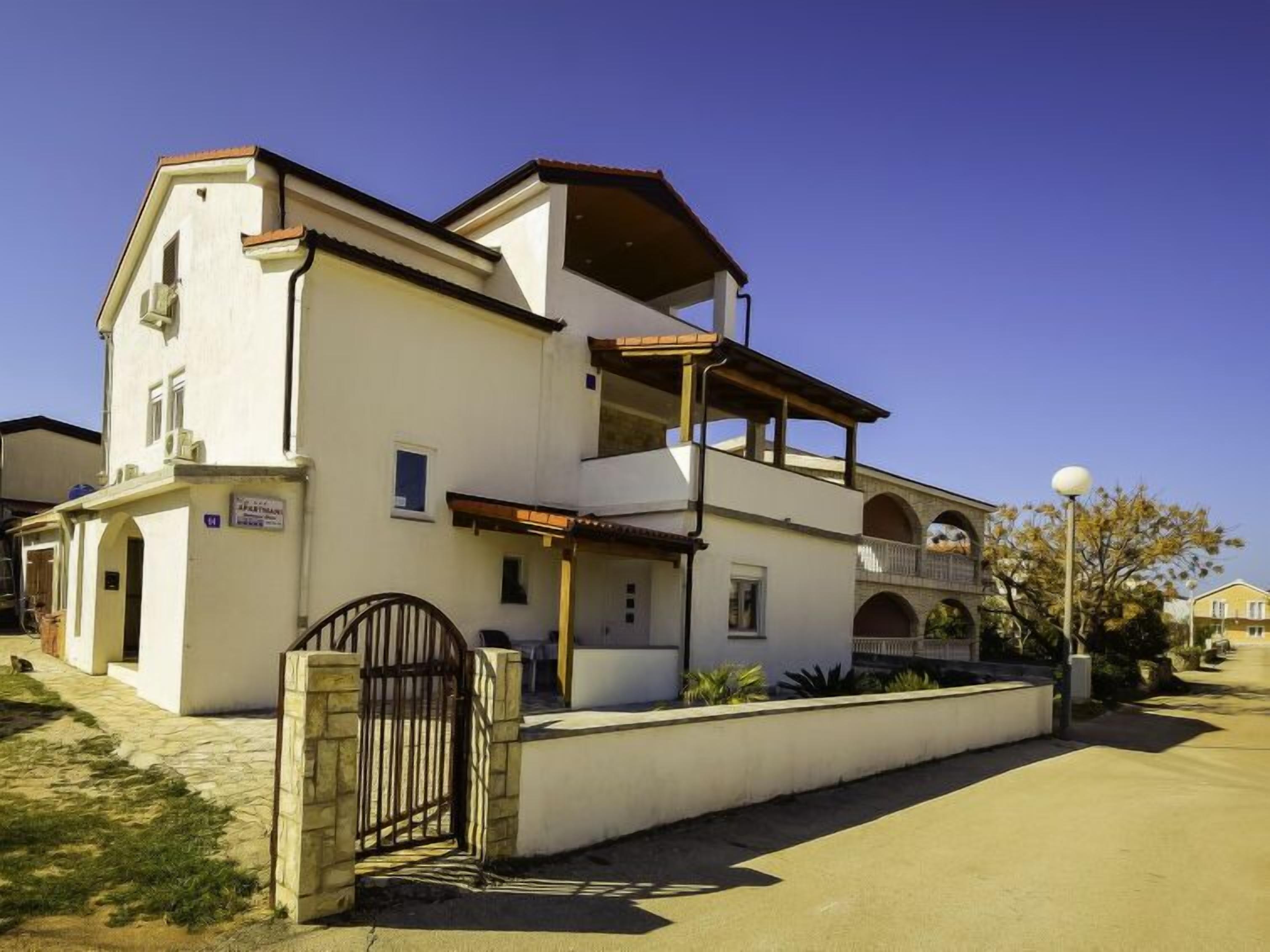 Un bâtiment à deux étages, doté d’un toit plat, d’un balcon à l’étage supérieur et d’une entrée fermée par un portail.