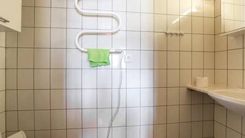 Een badkamer met witte betegelde wanden, een toilet, een douche met een witte slang en een groene handdoek hangend aan een haak.
