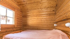Une pièce de cabane en bois comprenant un lit, une fenêtre et une lampe.