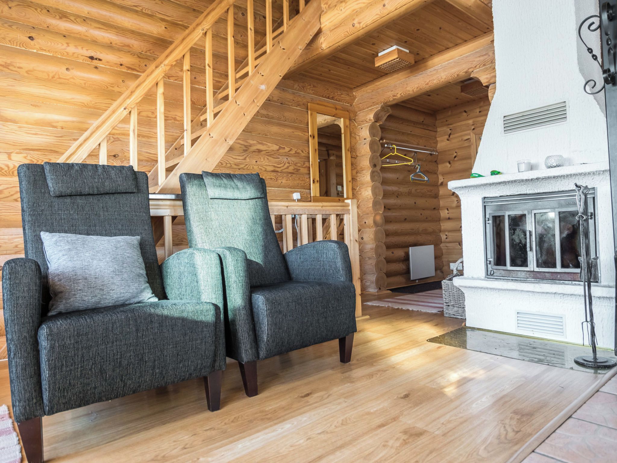A log cabin interior with two upholstered armchairs, a wooden staircase, and a fireplace.