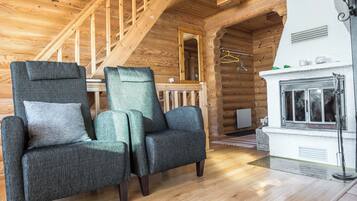 A log cabin interior with two upholstered armchairs, a wooden staircase, and a fireplace.