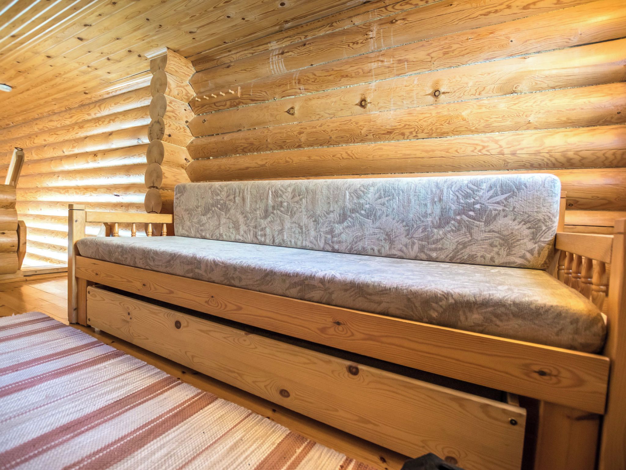 A log cabin interior with a sofa, wooden walls, and a striped rug.