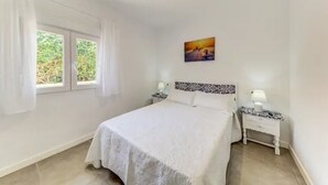 Ein Schlafzimmer mit einem großen Bett, zwei Nachttischen, einem Fenster mit Vorhängen und einem Gemälde an der Wand.