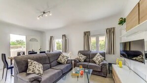 Ein modernes Wohnzimmer mit zwei grauen Sofas, einem Glastisch und einem Fernseher an der Wand.