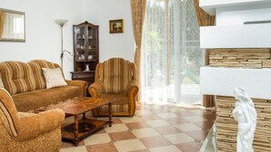 A living room with a sofa, armchair, and a small table. There is a cabinet, a lamp, and a statue on a pedestal. - Twin Combo by Interhome (Balatonboglar)