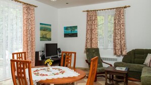 A cozy living room with a dining area, featuring a round table, chairs, a television, and a green sofa. - Twin Combo by Interhome (Balatonboglar)