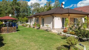 A single-story house with a tiled roof, a covered porch, and a small garden area with various plants and flowers. - Twin Combo by Interhome (Balatonboglar)