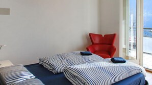 Ein Hotelzimmer mit einem Bett, zwei gestreiften Kissen, einem roten Sessel und einem großen Fenster mit Blick nach draußen.