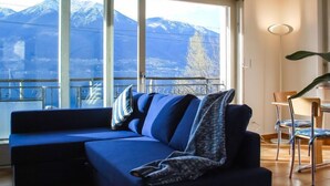 Ein modernes Wohnzimmer mit einer Couch, einem Esstisch mit Stühlen und Bergblick durch große Fenster.