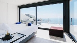 Un dormitorio moderno con una cama grande, una mesita de vidrio y vistas al mar.