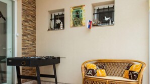 Ein Zimmer mit einem Kicker, einem Korbssessel mit gemusterten Kissen und zwei Wandregalen mit Dekoration.