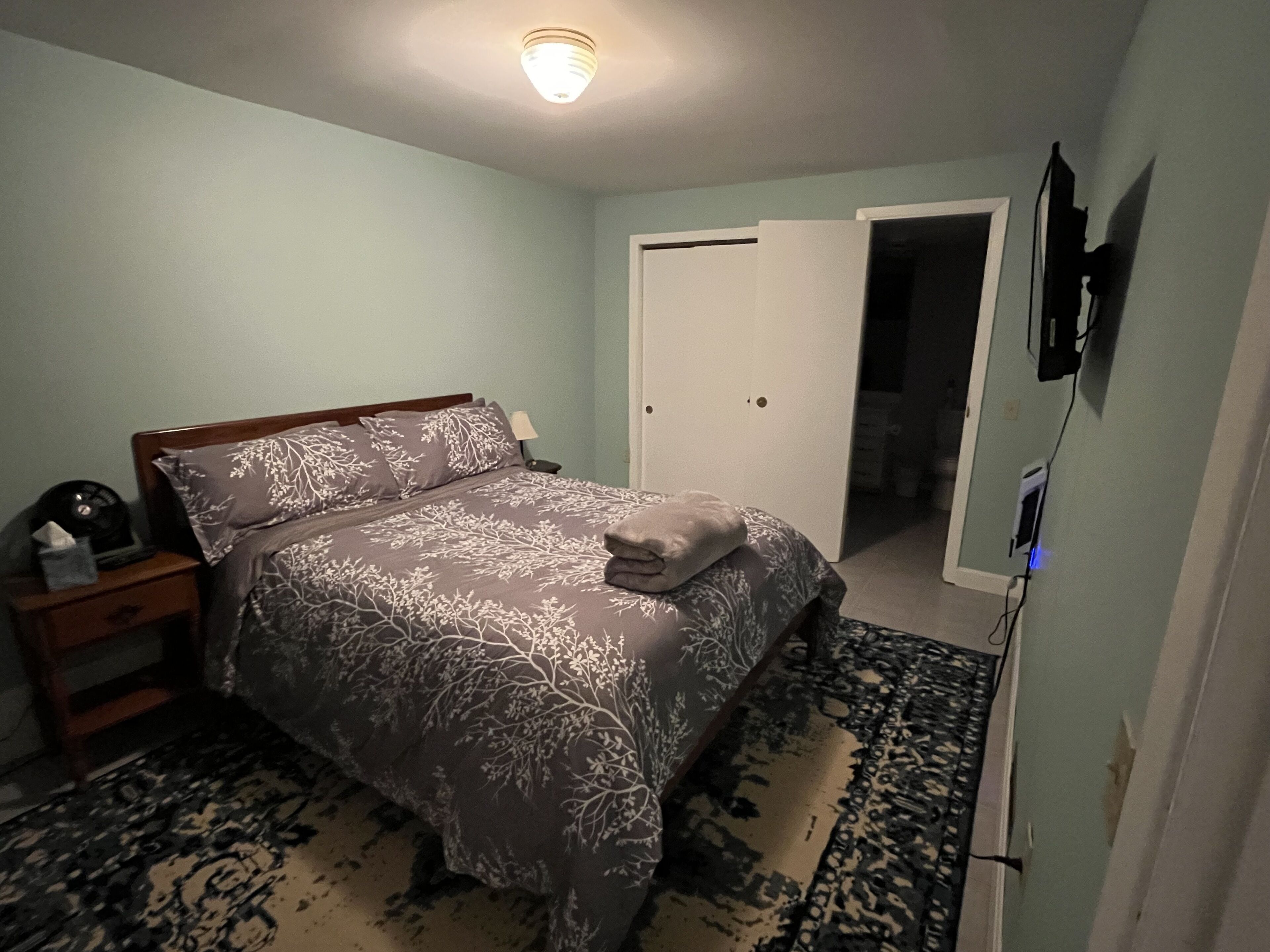 Une chambre à coucher comprenant un lit, une table de chevet et une porte donnant sur une autre pièce.
