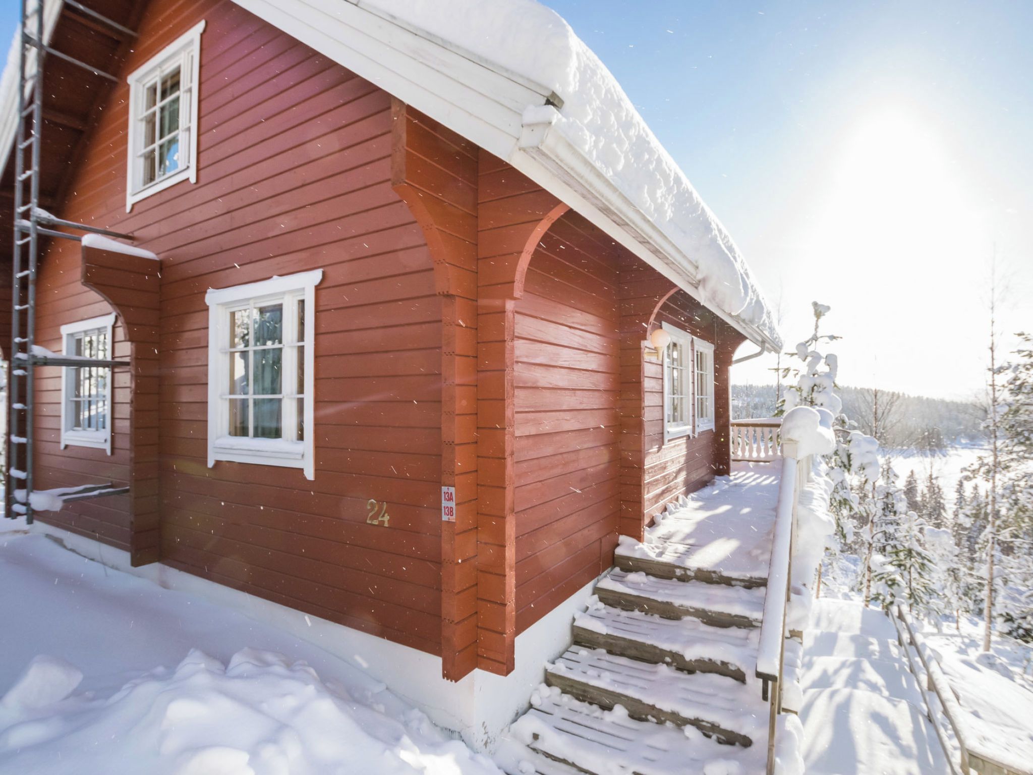 Une maison en bois rouge, avec un toit enneigé et des marches menant à un porche.