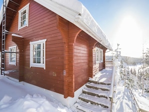 Une maison en bois rouge, avec un toit enneigé et des marches menant à un porche.