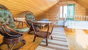 Une chambre confortable située dans les combles, avec des murs en bois et un plafond en pente. Elle comprend deux fauteuils à bascule, une petite table et un lit recouvert d’une courtepointe à rayures.