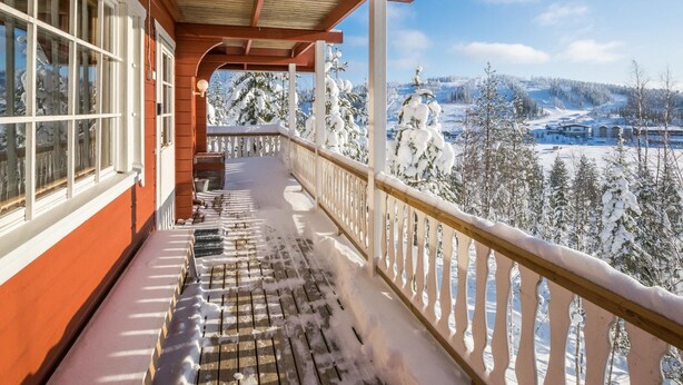 Un balcon en bois offrant une vue sur un paysage enneigé et, au loin, sur une station de ski.