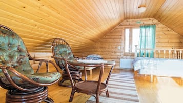 Tunnelmallinen ullakkohuone, jossa on puuseinät ja kalteva katto. Huoneessa on kaksi keinutuolia, pieni pöytä ja sänky, jonka päällä on ruutukuviollinen peitto.