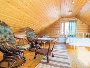 Une pièce mansardée chaleureuse avec des murs en bois et un plafond en pente. On y trouve deux fauteuils à bascule, une petite table et un lit recouvert d’une couverture à carreaux.