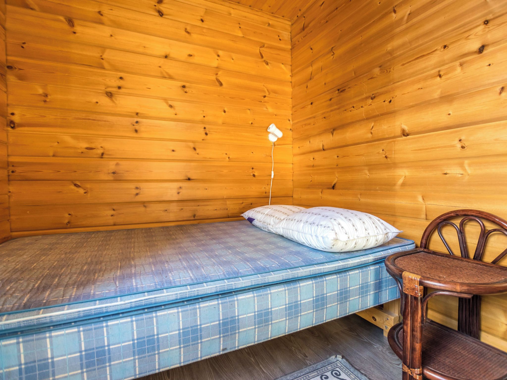 Une petite pièce en bois, aménagée comme une cabane, avec un lit simple, une chaise et une petite table.