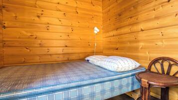 Une petite pièce en bois, aménagée comme une cabane, avec un lit simple, une chaise et une petite table.