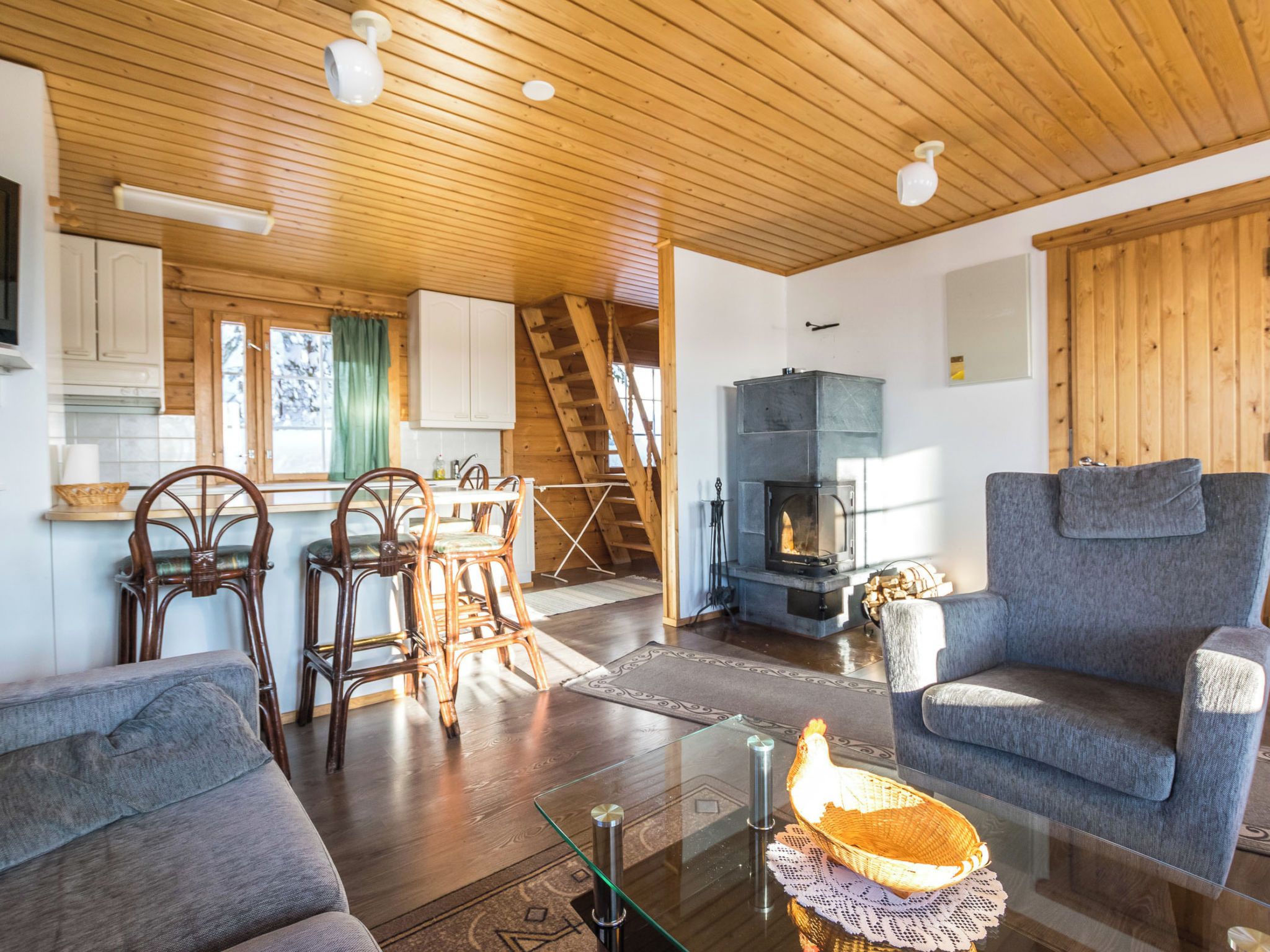 A cozy living room with a fireplace, wooden ceiling, and a dining area with chairs and a table.
