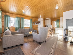 Un intérieur de chalet chaleureux avec un plafond en bois, une cheminée, un téléviseur et un coin repas.