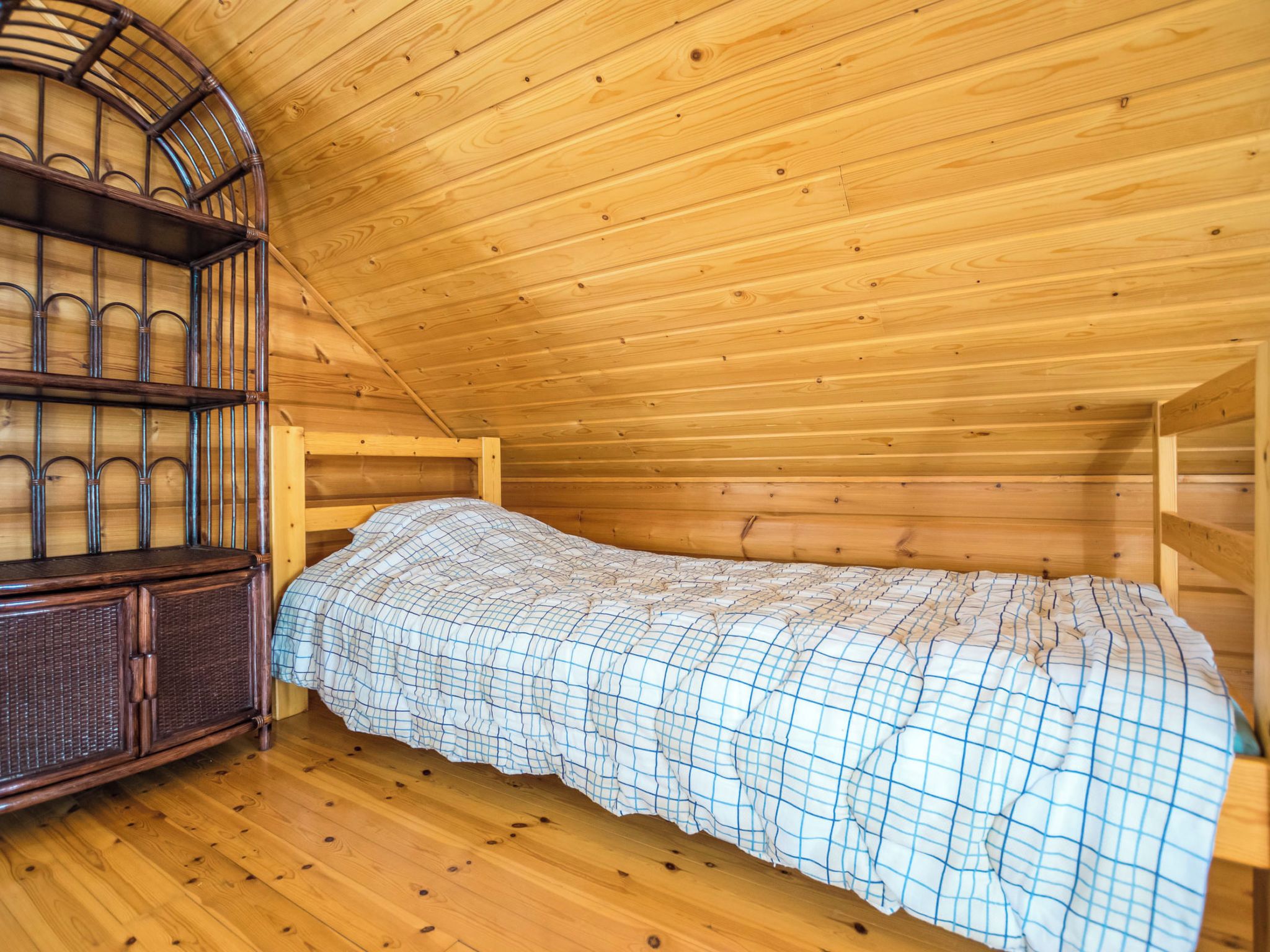 A single wooden bed in a cabin-style room with a sloped ceiling and a built-in wooden cabinet.