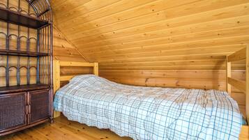 A single wooden bed in a cabin-style room with a sloped ceiling and a built-in wooden cabinet.