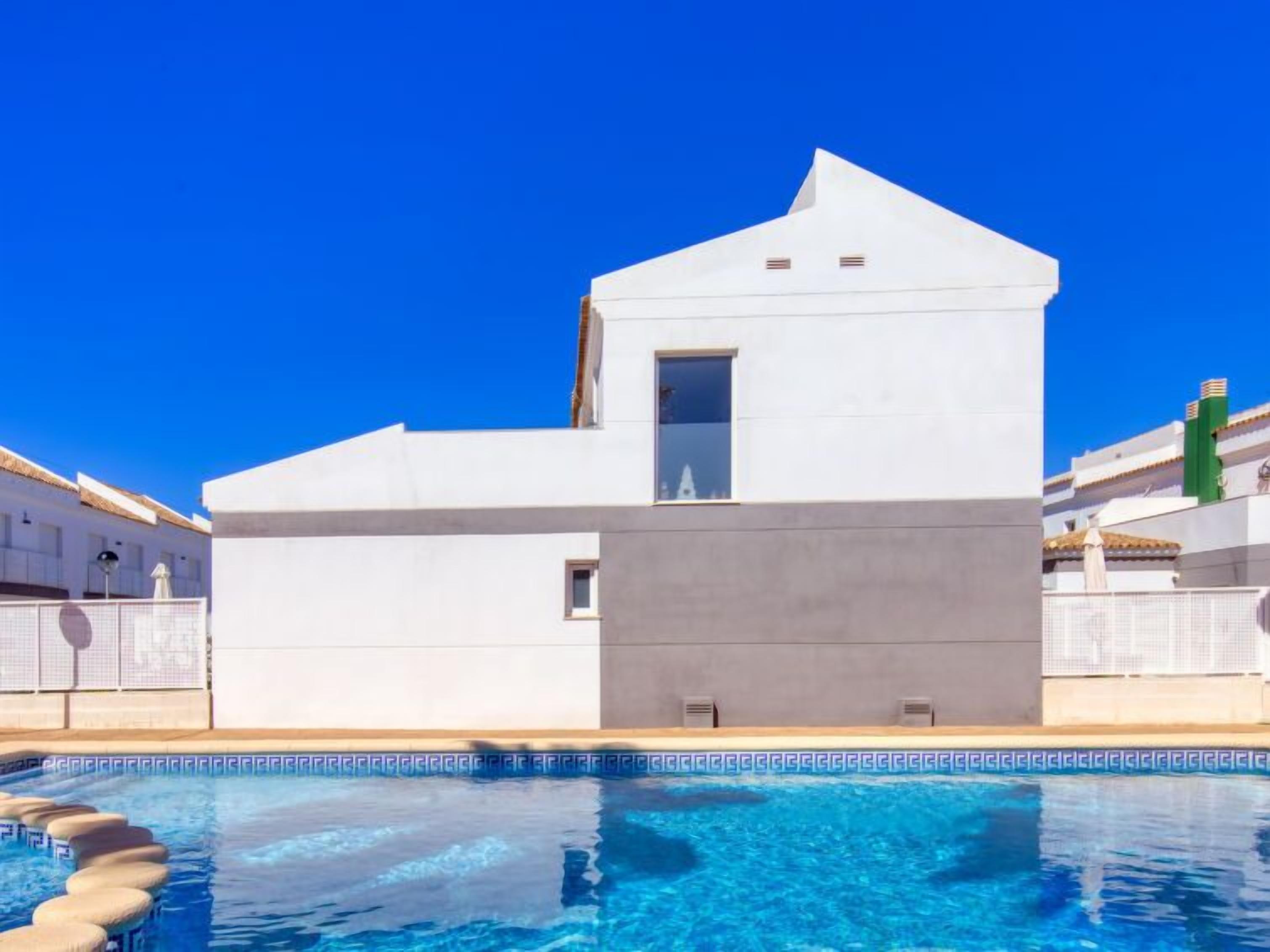 A modern white building with a pool in front.