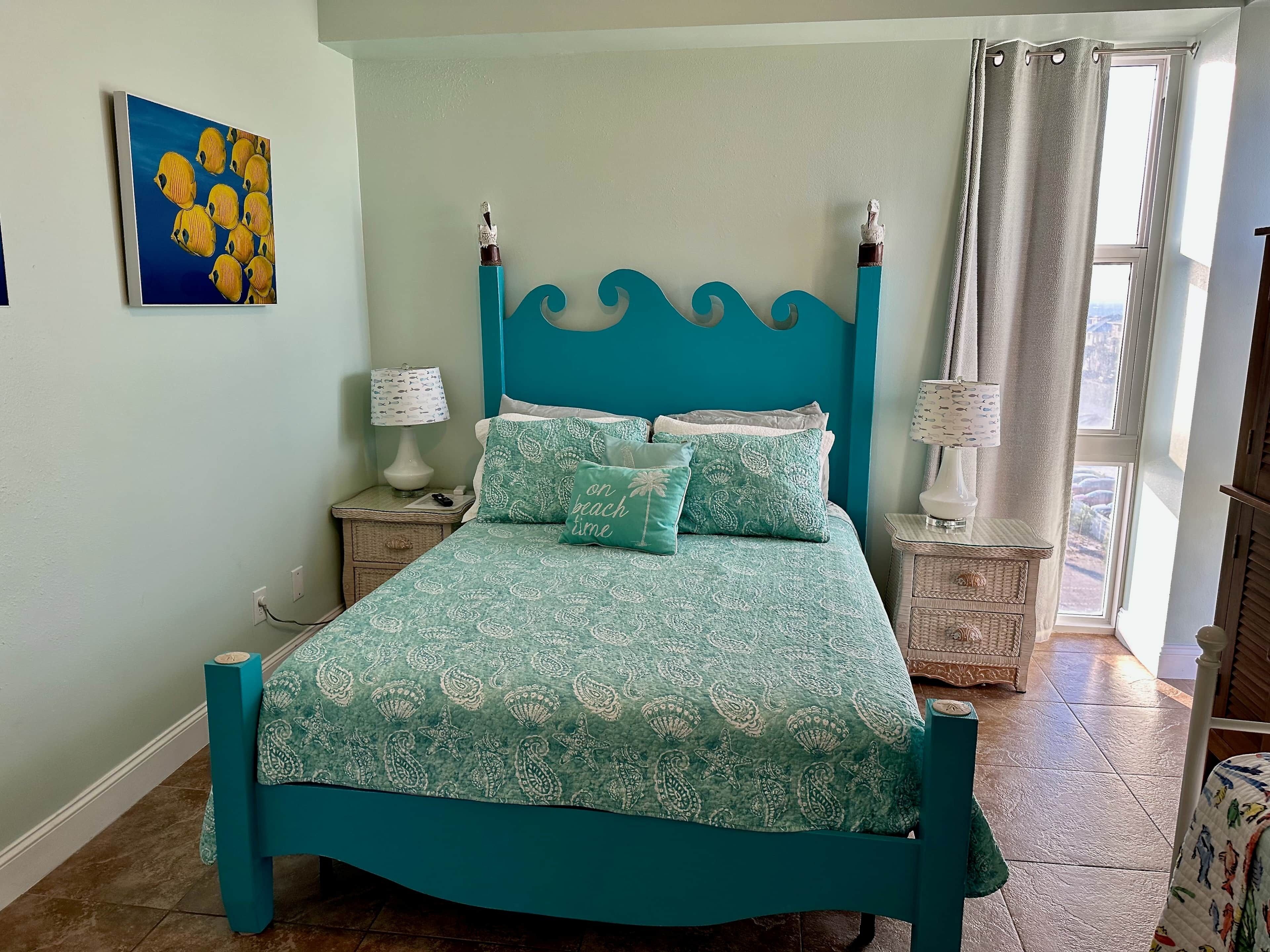 A teal-colored bed with patterned bedding, a headboard with a wave design, and two bedside tables with lamps.