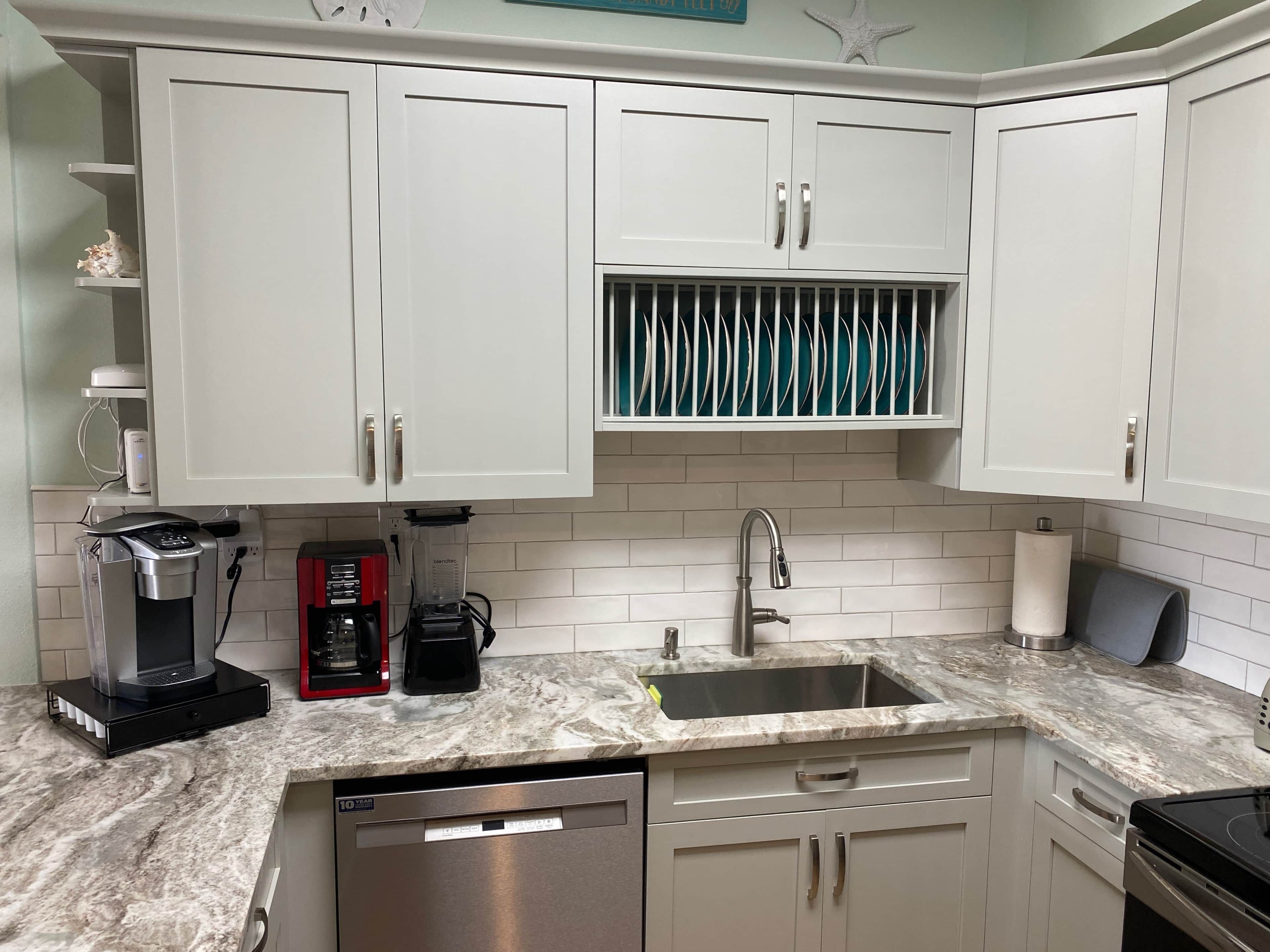 A kitchen with white cabinets, a built-in dishwasher, a coffee maker, and a sink with a marble countertop.