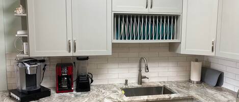 A kitchen with white cabinets, a built-in dishwasher, a coffee maker, and a sink with a marble countertop.
