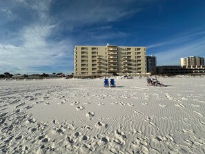 Um hotel à beira-mar com vários andares, uma praia arenosa em primeiro plano e céu claro.