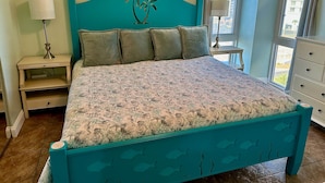 Un lit avec une couvre-lit à motifs floraux, une tête de lit turquoise et une table de chevet avec une lampe.
