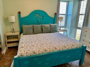 Un lit avec une couvre-lit à motifs floraux, une tête de lit turquoise et une table de chevet avec une lampe.